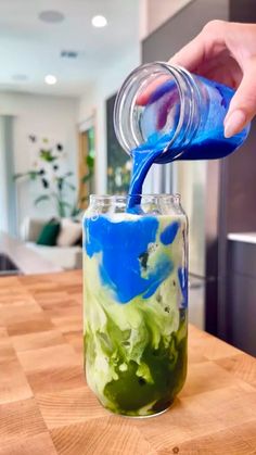 someone is pouring blue and green liquid into a jar