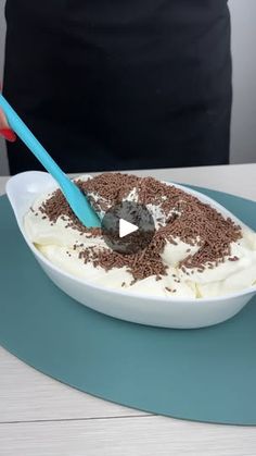 a person holding a spoon in a bowl filled with cream and chocolate