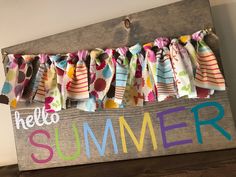 a wooden sign that says hello summer hanging from the side of a wall with colorful fabric on it