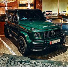 a green mercedes g class parked in front of a building with christmas lights on it