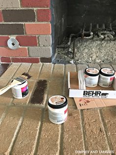 some paint cans are sitting on the floor next to a brick fireplace