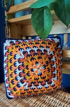 a crocheted pillow sitting on top of a wicker chair next to a potted plant