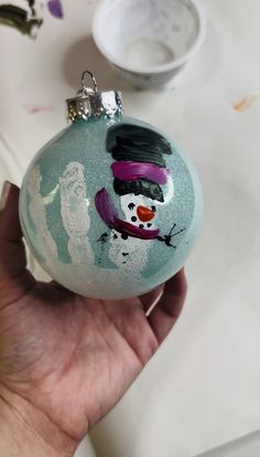 a hand holding a glass ornament with a snowman painted on it