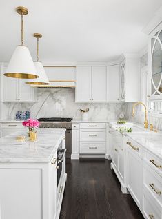 a white kitchen with marble counter tops and gold accents on the hood, along with an island