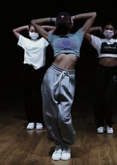 three young women wearing face masks while standing on a wooden floor in front of a black background