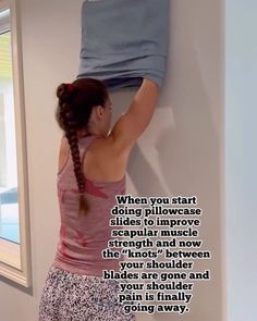 a woman hanging clothes on the wall with her hair in a ponytail and looking down