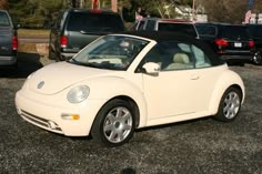 a white convertible car parked in a parking lot next to other cars and trucks on the street