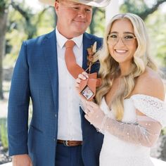 a woman in a white dress and cowboy hat holding a small award with a man in a blue suit standing next to her