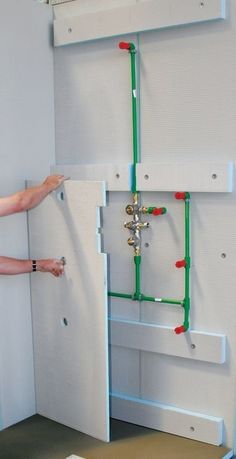 a man is working on an electrical panel in a room with white walls and green piping