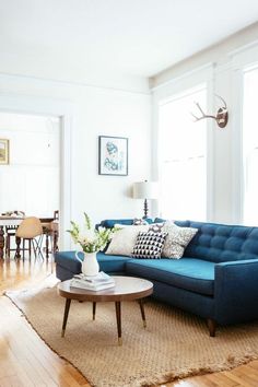 a living room with a blue couch and table in front of two large windows that have deer antlers on the wall