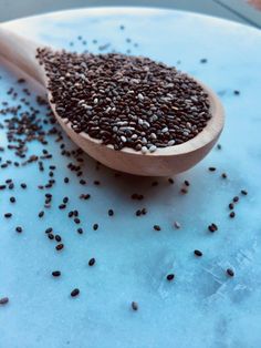 a wooden spoon filled with black seed on top of a blue countertop next to a pile of seeds