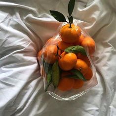 a plastic bag filled with oranges on top of a white bed cover covered in sheets