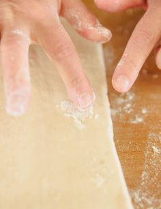 two hands reaching for dough on top of a wooden table