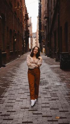 a woman is standing in an alleyway with her arms crossed and looking at the camera