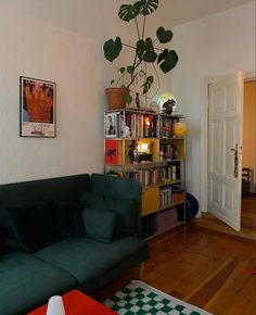 a living room filled with furniture and a book shelf next to a green couch on top of a hard wood floor