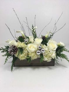 an arrangement of white flowers and greenery in a wooden vase with silver ornaments on top