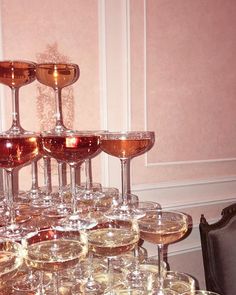 many glasses of wine are lined up on a table in front of a pink wall