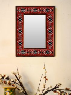 a mirror hanging on the wall above a vase with flowers and branches in front of it