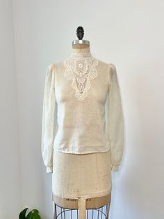 1970s Gunne Sax sheer cotton ivory long sleeve blouse with button down closure down the back middle. This shirt has a gorgeous floral lace mock neck that continues down the front middle.  In very good vintage condition, minor discoloration by armpit it hardly noticeable! B: 34" W: 31" L: 22" Vintage Beige Blouse For Spring, Fitted Off White Long Sleeve Blouse, Fitted Off White Blouse With Long Sleeves, Vintage White Blouse For Spring, Vintage Cream Top For Fall, Cream Long Sleeve Sheer Top, Long Sleeve Sheer Cream Top, 1970s Long Sleeve Blouse, Vintage Cream Blouse