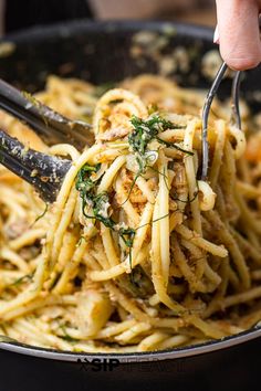 someone is holding a fork full of pasta with parsley on top, in a skillet