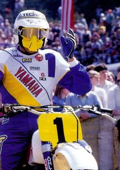 a man riding on the back of a yellow and purple motorcycle in front of a crowd