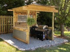 an outdoor kitchen with grill and bbq in the middle of a garden area next to a wooden fence