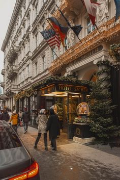 people are walking down the street in front of a building with christmas decorations on it