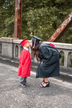 a woman in a graduation gown kissing a little boy wearing a red cap and gown