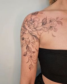 a woman wearing a black top with flowers on her shoulder and arm tattooing it