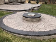 a fire pit sitting on top of a lush green field next to a stone patio