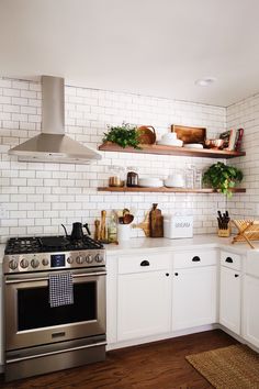 a kitchen with white cabinets and open shelving on the wall above the stove top