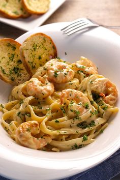 pasta with shrimp and garlic bread on a white plate in front of two slices of bread