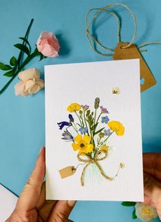 a person holding up a card with flowers on it and some string attached to it