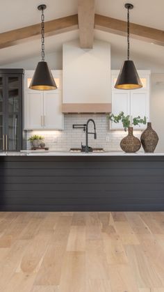 a large kitchen with wooden floors and white cabinets, two pendant lights over the island