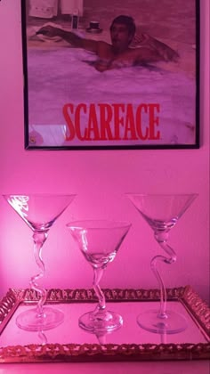 three martini glasses sitting on top of a tray in front of a pink wall with a poster above it