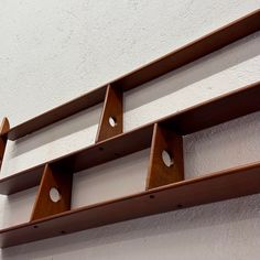 three wooden shelves with holes in them against a white wall