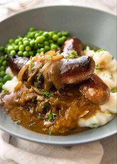 a plate with mashed potatoes, peas and sausages on it in gravy