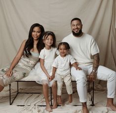 a man and two children sitting on a bed in front of a white backdrop with a curtain