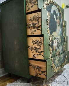 a green dresser with drawers and pictures on the front, painted gold leaf design inlays