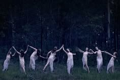 a group of women dancing in the woods at night with their arms extended and hands raised