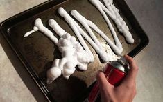 someone is decorating white candles on a baking sheet with red paint and a can