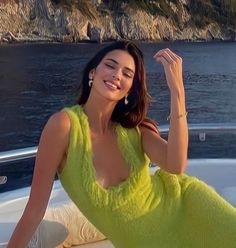 a woman sitting on the back of a boat in a green dress and diamond earrings