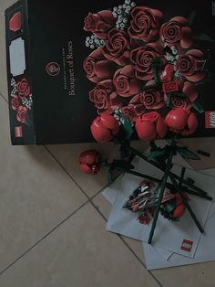 there is a box with roses on it next to some papers and flowers in the middle