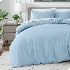 a bed with blue sheets and pillows in a room next to a potted plant