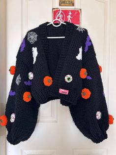 a black sweater with orange and purple buttons hanging on a door hanger in front of a white door