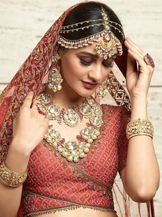 a woman in a red and gold bridal outfit with jewelry on her head,