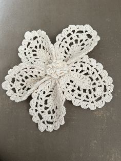 a crocheted white flower on a gray table top with the petals folded down and ready to be sewn