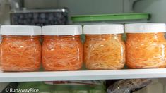 four jars filled with shredded carrots sitting on top of a shelf