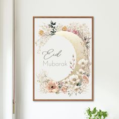 a white wall with a floral frame hanging on it's side next to a potted plant