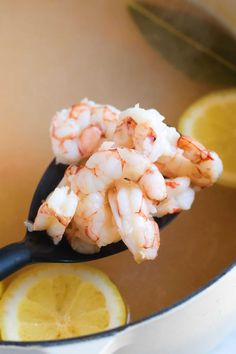 a spoon full of shrimp with lemon wedges